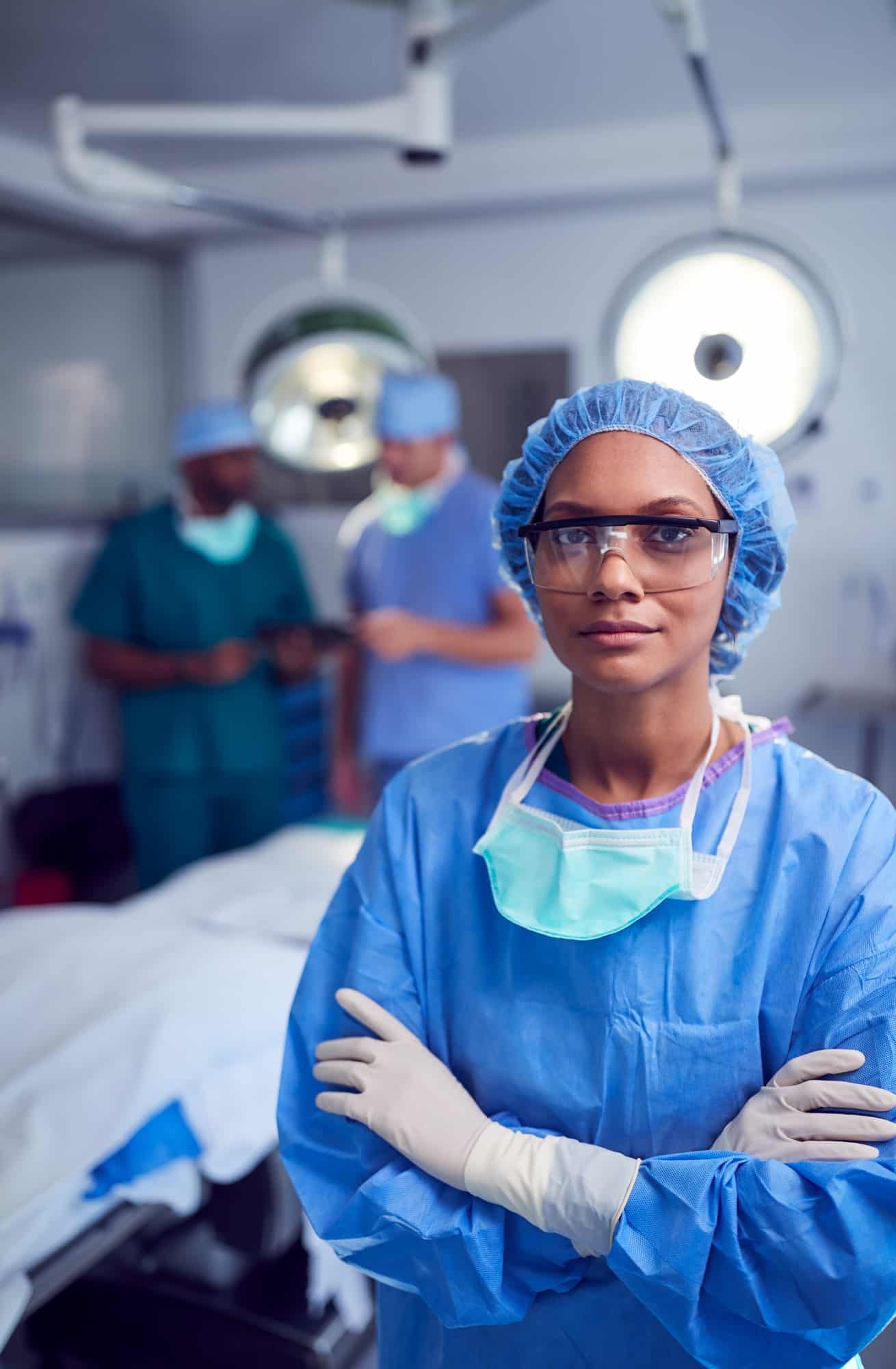 Portrait Of Female Surgeon Wearing Scrubs And Protective Glasses In Hospital Operating Theater