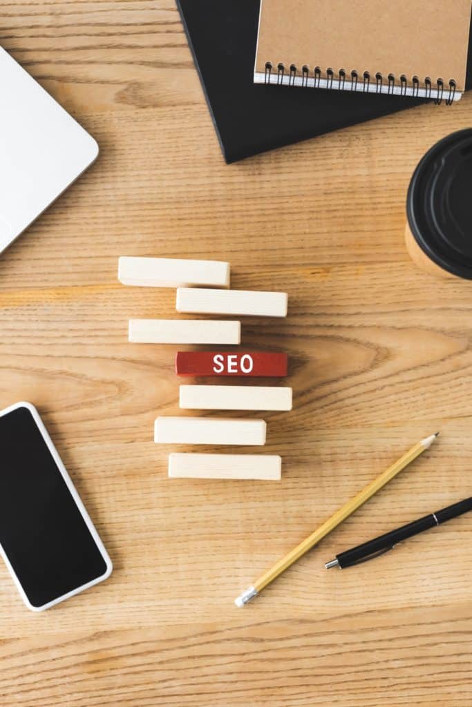 top view of smartphone, paper cup, notebooks, pen, pencil and wooden rectangles with lettering seo