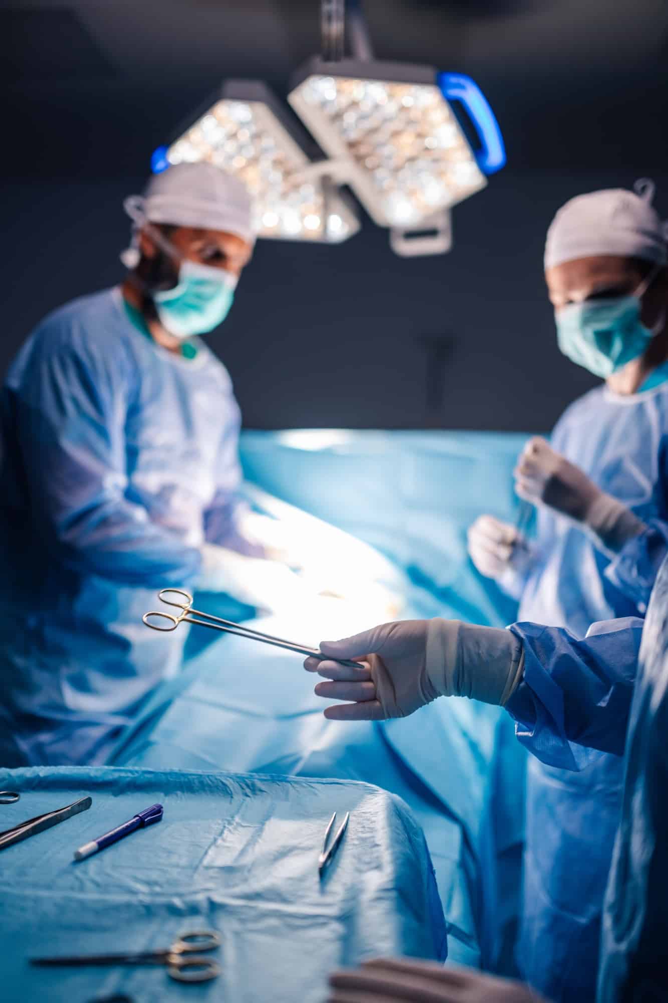 Surgeon handing surgical tool to another in sterile operating room.